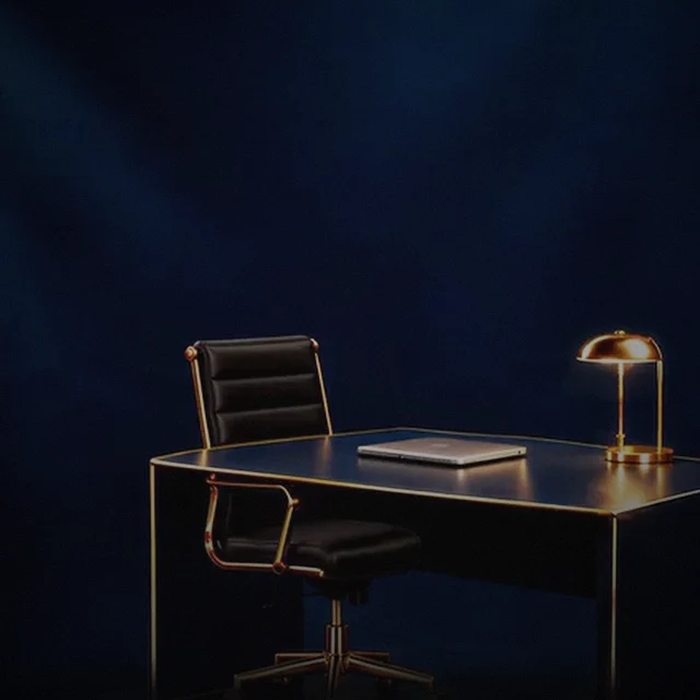 Agent Kelly in a black suit and sunglasses sits down at a navy and gold desk, opens a laptop and starts typing